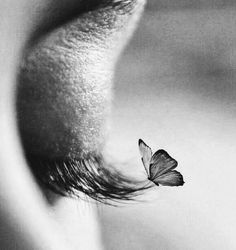 a black and white photo of a butterfly flying over the eye of a woman's face