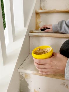 a person holding a yellow bowl with food in it on the steps next to some stairs