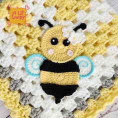 a crocheted yellow and white blanket with a small bee on it's chest