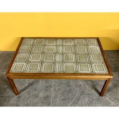 a wooden table with a green and white pattern on the top sitting in front of a yellow wall