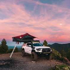 a truck parked on top of a mountain under a red and white tent at sunset