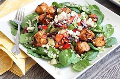 a salad with spinach, chicken and cranberries in a bowl on a white table