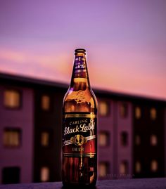 a bottle of beer sitting on top of a wooden table next to a purple building