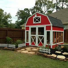 a small red and white shed sitting in the middle of a grass covered yard next to a wooden fence