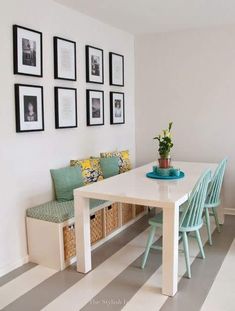 a dining room table with blue chairs and pictures on the wall above it, next to a bench