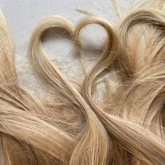 some very long blonde hair laying next to each other on a white surface with a heart shaped cut in the middle