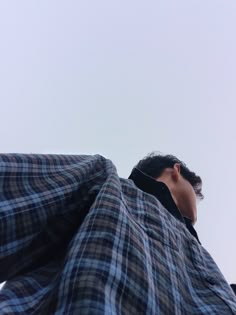 the man is wearing a plaid jacket and looking up at the sky with his head tilted back