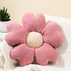 a pink flower shaped pillow sitting on top of a white bed next to a potted plant