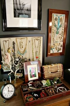 an assortment of jewelry sits on a table in front of two framed pictures and a clock