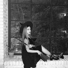 a woman sitting on a window sill wearing a witch costume