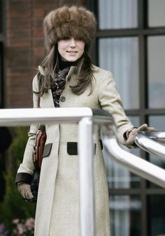 a woman wearing a fur hat and coat standing next to a white rail with her hand on the railing