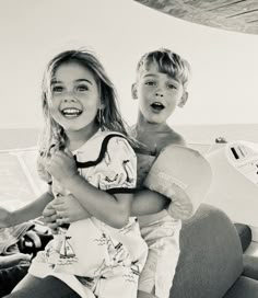 two young children sitting on the back of a boat in the ocean, one holding his arm around the other