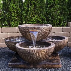 an outdoor fountain with three bowls and water running down it's sides in front of a brick wall