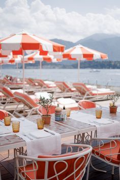 an outdoor dining area with orange and white umbrellas over the water's edge