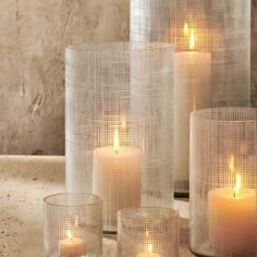 some candles are sitting on a table next to vases with mesh wrapped around them