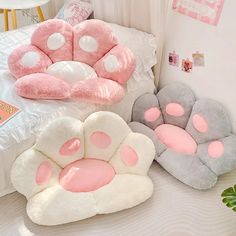 three pillows with pink and grey designs on them sitting on top of a white bed