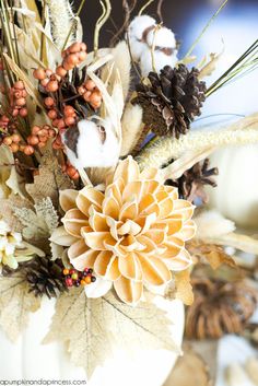 a white vase filled with lots of different types of flowers and leaves on top of a table