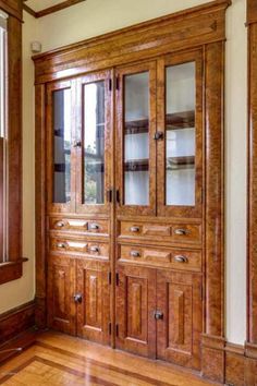 a large wooden cabinet with glass doors and drawers in a room that has hardwood floors