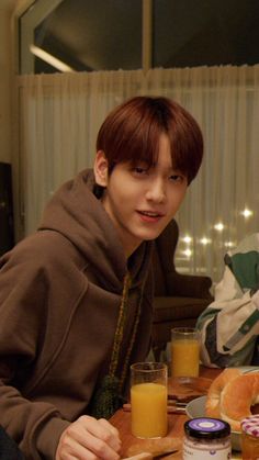 a young man sitting at a table with orange juice and bread in front of him