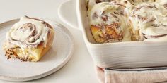 a white plate topped with a cinnamon roll next to a casserole dish covered in icing