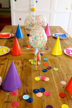 colorful party hats and confetti on a wooden table with plates, napkins and balloons