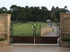 an iron gate with a monogrammed w on it and a driveway in the background