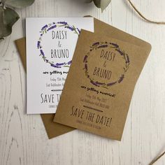 two wedding save the dates cards on top of each other next to some greenery