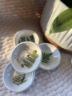 four bowls with plants painted on them sitting next to a potted plant in the background