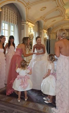 a group of women standing next to each other in front of a mirror wearing dresses