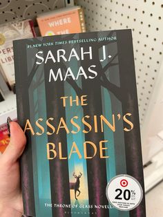 a person holding up a book in front of bookshelves with the title, the assassin's blade