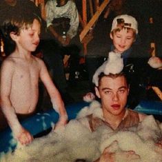 two boys and an older man are in the tub with soap on their heads, while another boy is wearing a sailor's hat