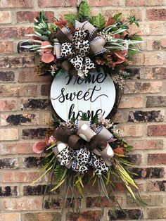 a sign that says home sweet home hanging on the side of a brick wall next to flowers