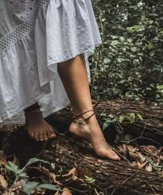 a woman standing on top of a tree trunk in the middle of a forest with her bare feet