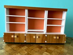 a wooden bookcase with two doors and three drawers on the bottom, in front of a blue wall