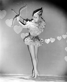 an old photo of a woman holding a bow and arrow with hearts in the background