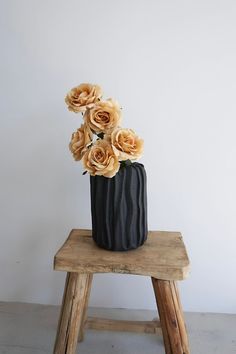 a black vase filled with flowers sitting on top of a wooden stool