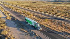 a green and white truck driving down a road in the middle of an open field