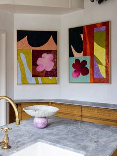 two paintings hang on the wall above a sink in a room with marble counter tops