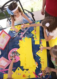 three children are sitting at a table making crafts with construction paper and beads on it