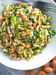 a white bowl filled with salad and nuts on top of a wooden table next to a fork