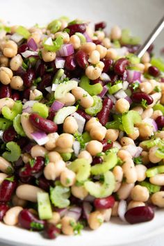 a salad with beans, celery and onions on a white plate next to a fork