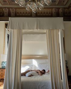 a man laying on top of a white bed under a chandelier