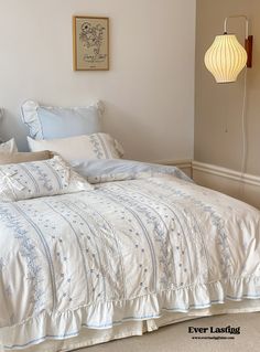 the bed is made with white linens and blue embroidered sheets, along with two lamps on either side