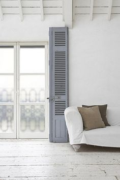 a white couch sitting in front of a window next to a wooden floor and shutters