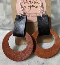 the earrings are made from wood and have black leather on them, with a thank you sign