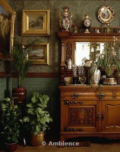 there is a wooden cabinet in the room with potted plants and pictures on the wall