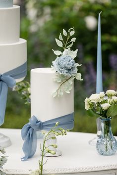 three tiered wedding cakes with blue ribbons and flowers in vases next to each other