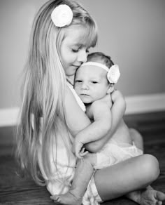 a woman holding a baby in her arms while sitting on top of a wooden floor