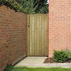 a wooden gate in front of a brick wall and shrubbery on the side of a building