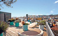 an outdoor deck with potted plants on it and buildings in the background at daytime